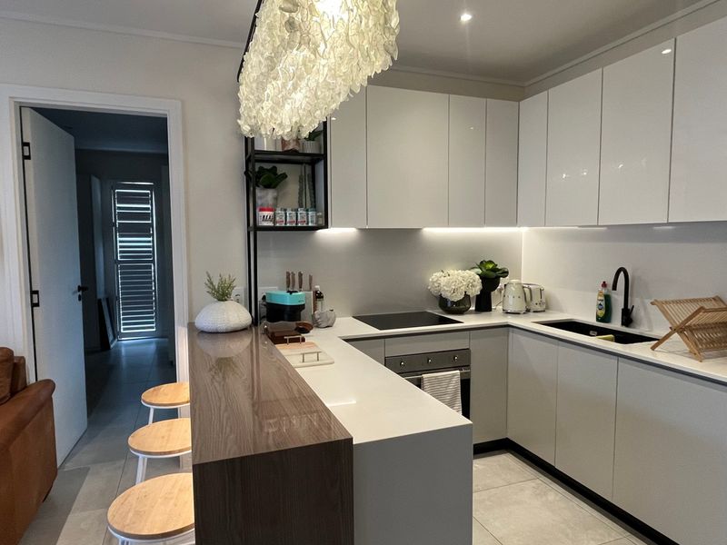 Modern kitchen featuring sleek white cabinetry, stone countertops, a breakfast bar, integrated appliances, and under-cabinet lighting, creating a clean and functional culinary space.