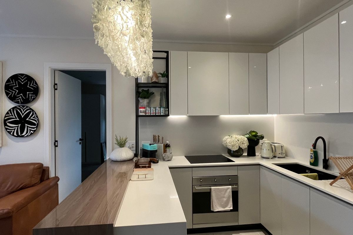 Modern kitchen featuring sleek white cabinetry, stone countertops, integrated appliances, and a functional breakfast bar with contemporary lighting.