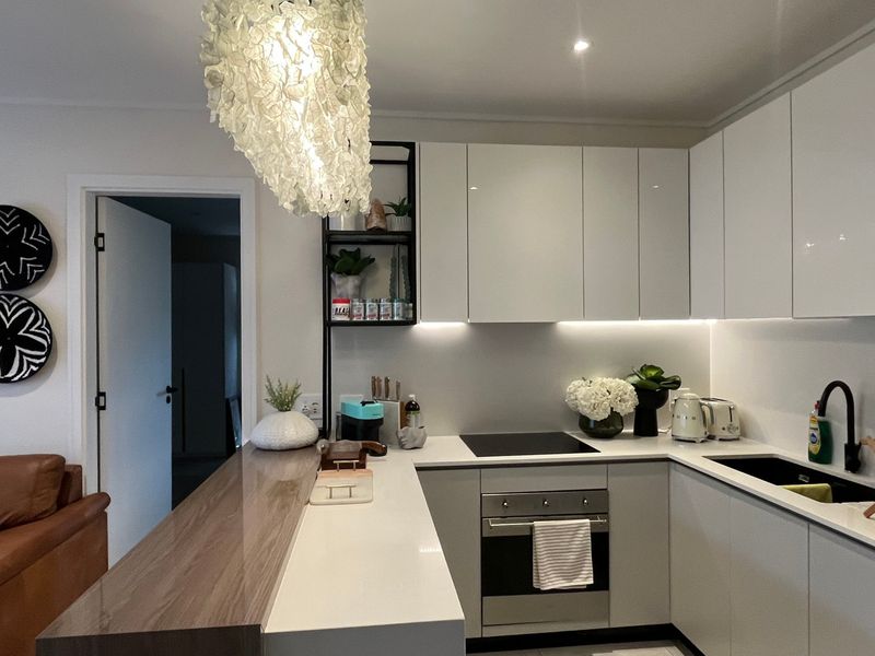 Modern kitchen featuring sleek white cabinetry, stone countertops, integrated appliances, and a functional breakfast bar with contemporary lighting.