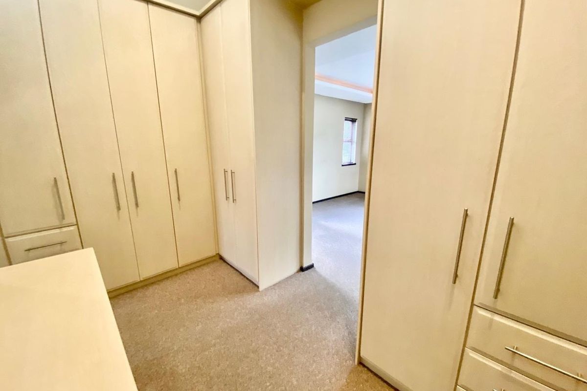 A spacious bedroom area featuring extensive built-in cupboards and neutral carpeting, offering ample storage and a clean, functional layout.