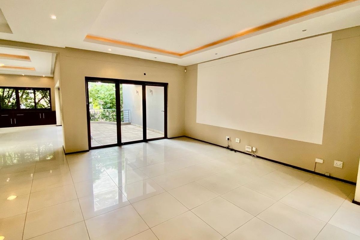 Spacious, light-filled living area featuring polished porcelain floor tiles, recessed ceiling lighting with cove accents, and large sliding glass doors leading to a patio.