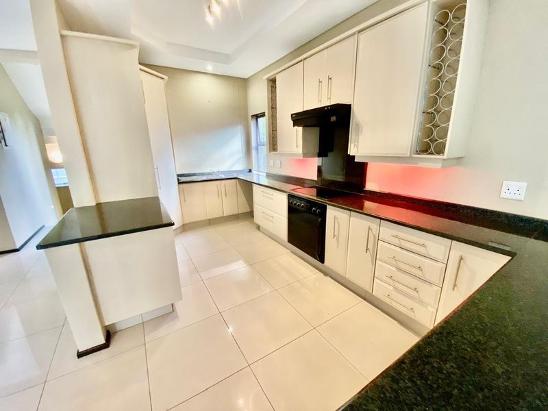 Modern kitchen featuring sleek white cabinetry, dark granite countertops, integrated oven, extractor fan, and tiled flooring in a clean, open-plan layout.
