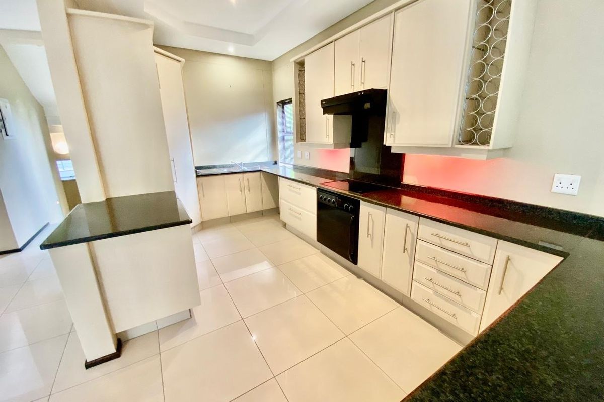Modern kitchen featuring sleek white cabinetry, dark granite countertops, integrated oven, extractor fan, and tiled flooring in a clean, open-plan layout.
