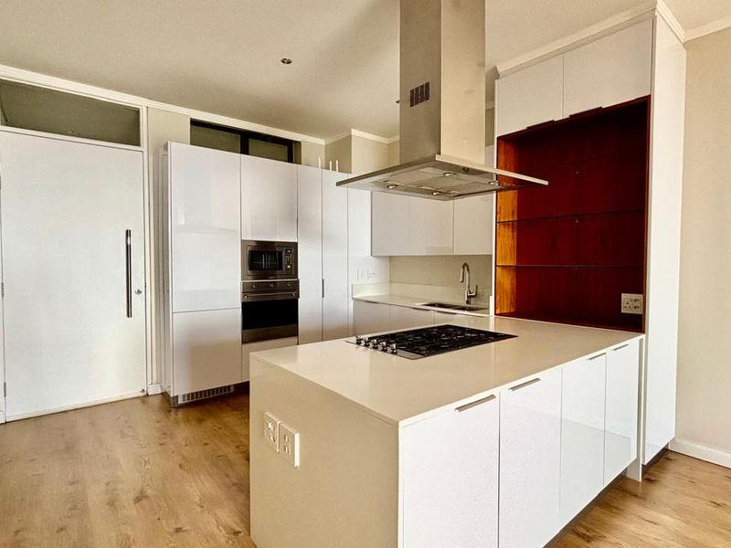 Modern kitchen featuring a central island with a gas hob, built-in oven, microwave, sleek white cabinetry, and high-quality laminate flooring.