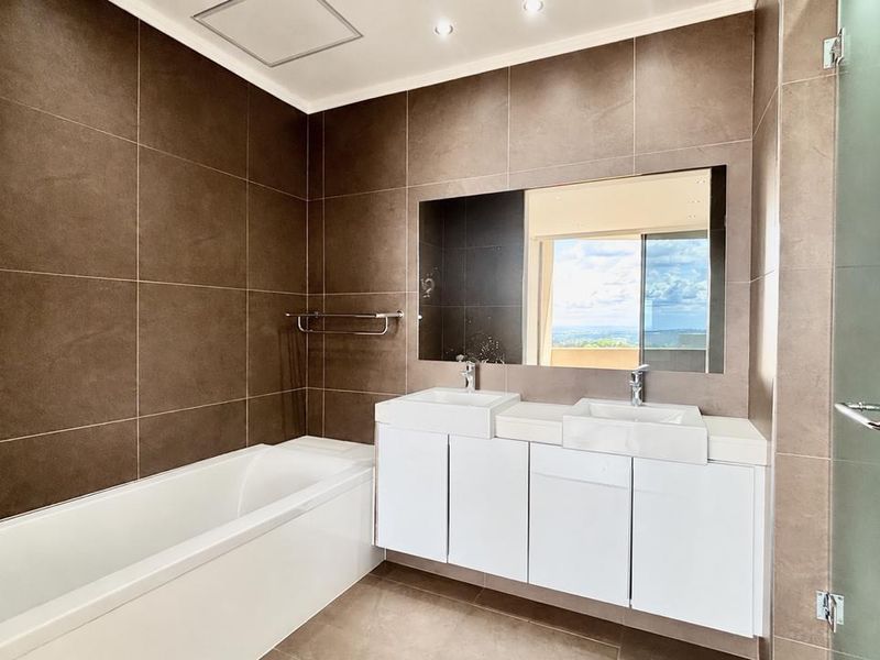 Modern bathroom featuring a double vanity, built-in bathtub, large wall mirror, and floor-to-ceiling tiling with a glass-enclosed shower.