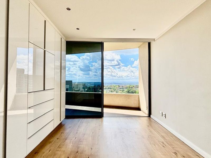 Bright bedroom featuring modern built-in cupboards, laminate flooring, and a sliding glass door opening onto a private balcony with scenic views.