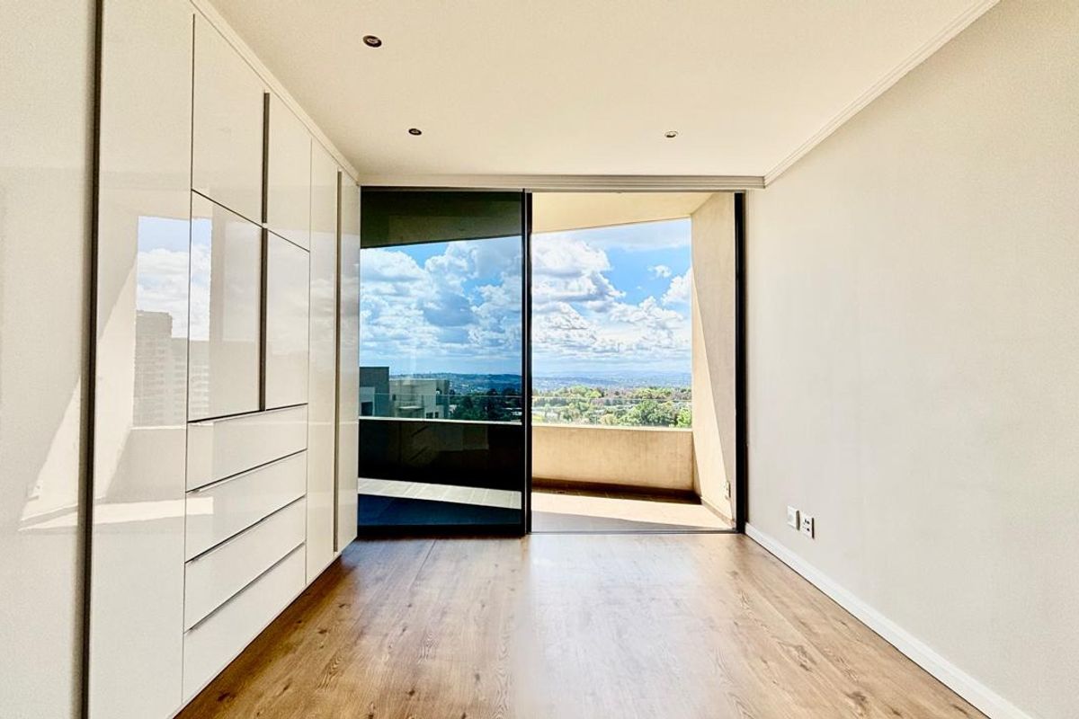 Bright bedroom featuring modern built-in cupboards, laminate flooring, and a sliding glass door opening onto a private balcony with scenic views.