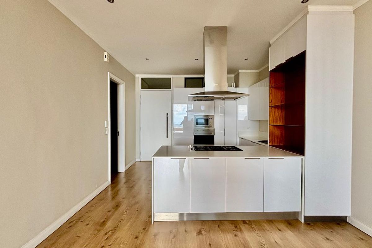Modern kitchen featuring a central island, built-in oven, extractor fan, and sleek white cabinetry with integrated shelving, set against light wood-look flooring.