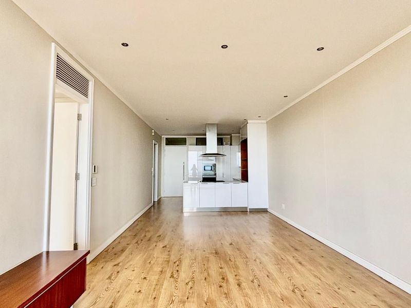 Spacious open-plan living area featuring laminate flooring, recessed lighting, and a modern kitchen with built-in cabinetry and integrated appliances.