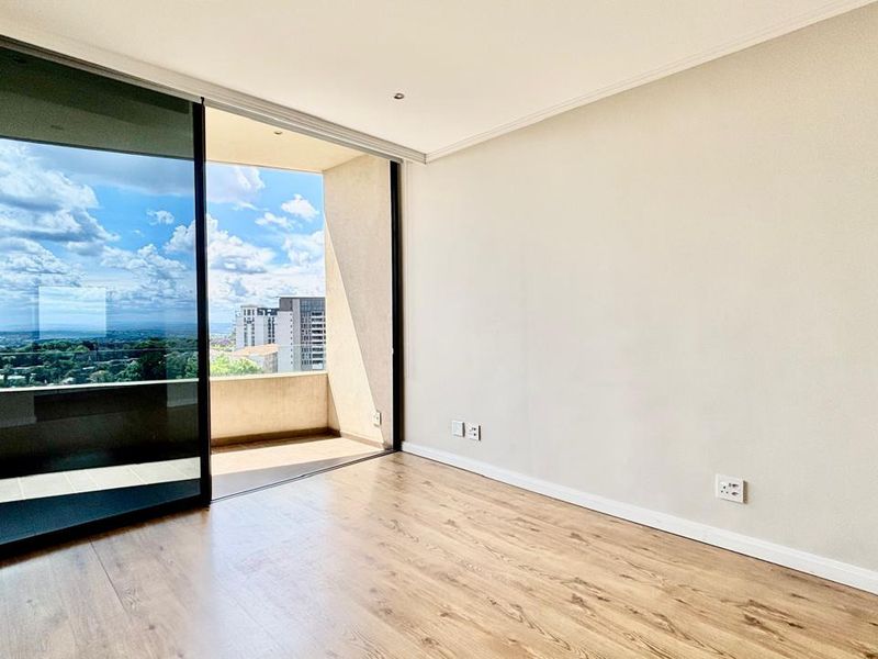 Bright and spacious living area featuring modern laminate flooring, recessed lighting, and a large sliding glass door opening onto a private balcony with city views.