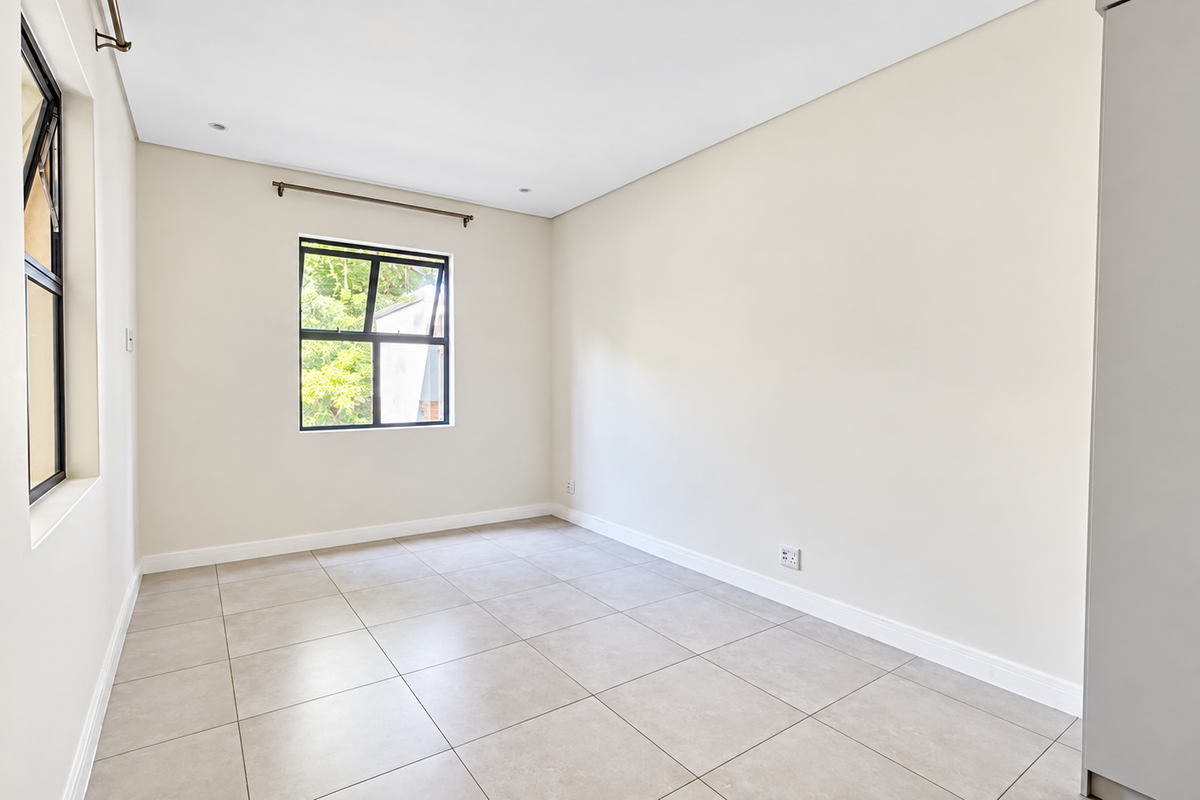 A bright and spacious empty bedroom featuring neutral tiled flooring, built-in cupboards, and modern aluminium window frames.