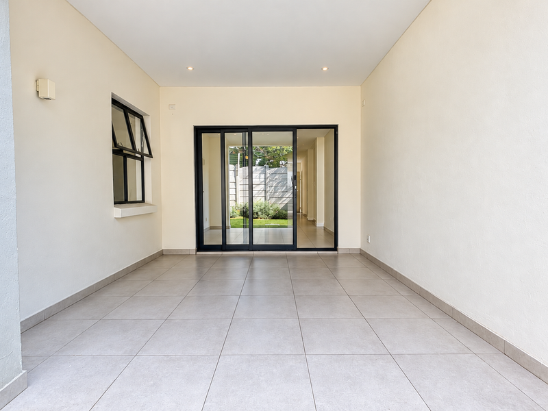 A clean, covered patio area featuring neutral floor tiles, recessed lighting, and large sliding glass doors providing access to the interior living space.