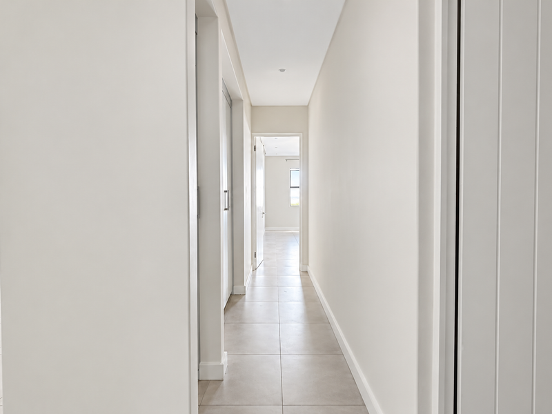 A bright and neutral hallway featuring clean tiled flooring, recessed lighting, and access to multiple rooms within the apartment.