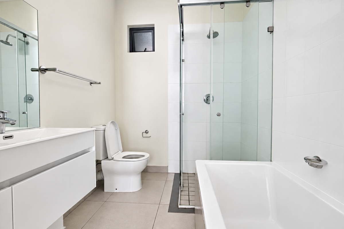 A clean, modern bathroom featuring a white vanity, a separate shower enclosure with glass doors, a bathtub, and neutral tiled finishes throughout.