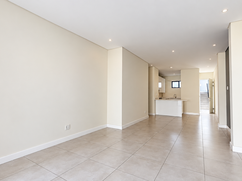 A bright and spacious open-plan living area featuring neutral tiled flooring, recessed lighting, and a modern kitchen with a central island.
