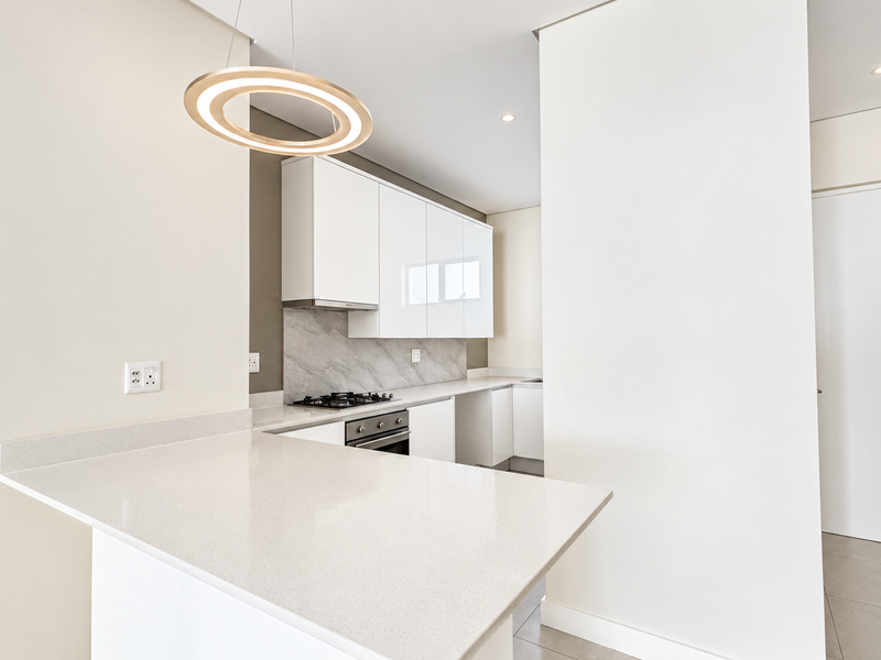 Modern kitchen featuring sleek white cabinetry, stone countertops, a gas hob, and a stylish marble-look splashback in a clean, minimalist design.