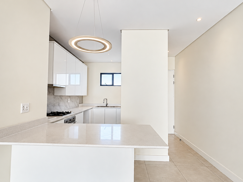 Modern open-plan kitchen featuring sleek white cabinetry, quartz countertops, integrated gas hob, and high-quality tiled flooring in a bright, minimalist space.