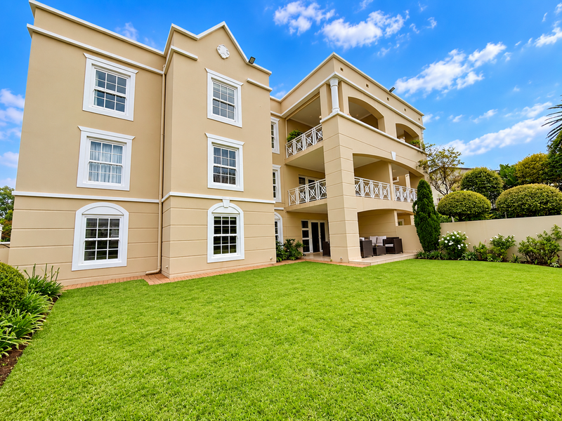 A well-maintained multi-story rear facade featuring classic sash windows, covered patio areas, and a spacious, manicured lawn.