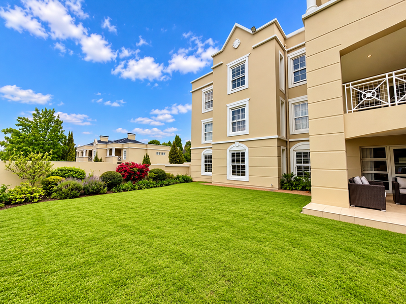 A well-maintained rear garden featuring a lush green lawn, landscaped borders, and a covered patio area attached to the multi-story residential building.