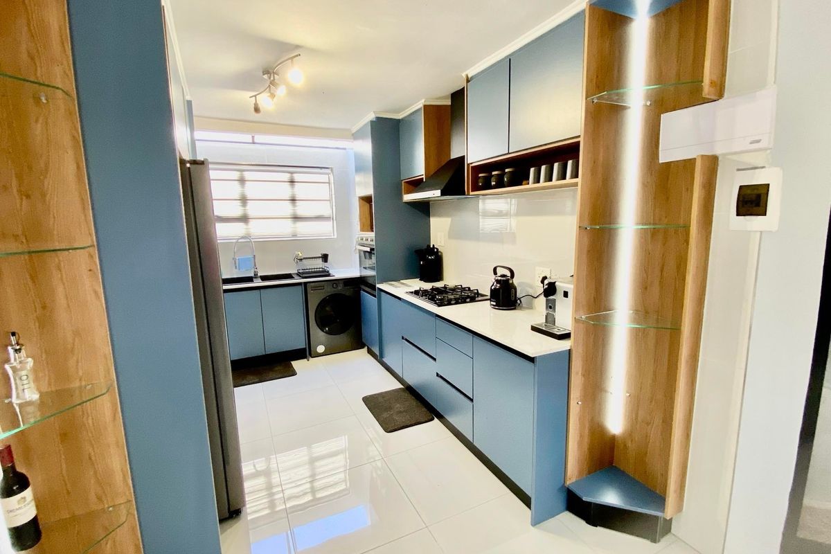 Modern kitchen featuring blue cabinetry, white countertops, gas hob, extractor fan, and integrated shelving with built-in lighting.