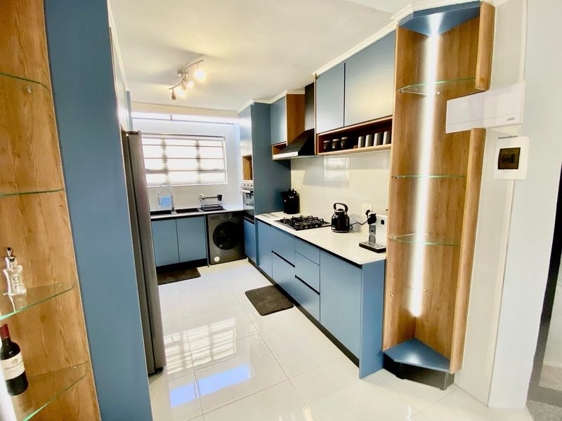 Modern kitchen featuring blue cabinetry, white countertops, gas hob, extractor fan, and integrated shelving with built-in lighting.