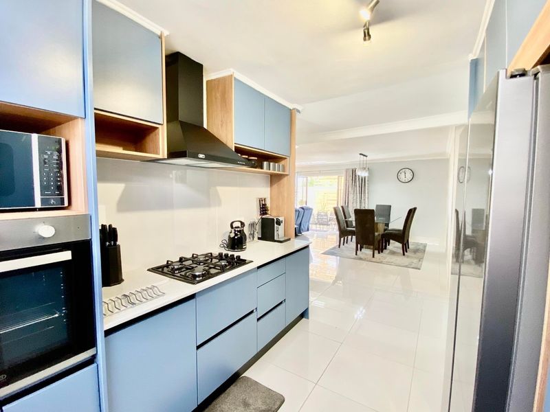 Modern open-plan kitchen featuring sleek blue cabinetry, built-in appliances, and polished tiled flooring, flowing seamlessly into the adjacent dining area.