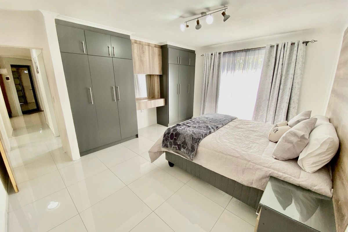 A modern bedroom featuring sleek grey built-in cupboards, a integrated vanity unit, polished floor tiles, and contemporary track lighting.