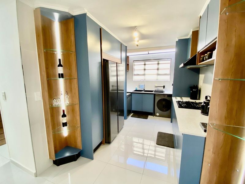 Modern kitchen featuring blue cabinetry, stone countertops, a gas hob, extractor fan, and integrated shelving with built-in lighting.
