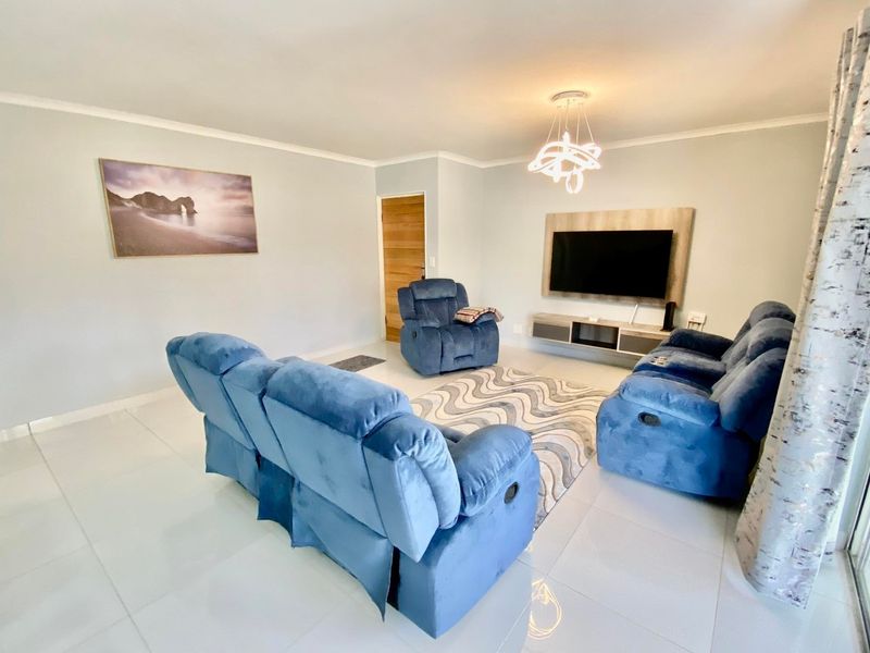 A bright and well-maintained living room featuring large format floor tiles, a modern pendant light, and a built-in media console.
