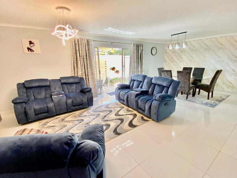 Spacious open-plan living and dining area featuring polished floor tiles, a marble-effect feature wall, and direct access to the patio through sliding glass doors.