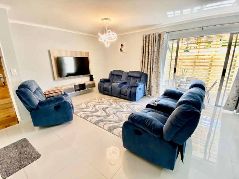 A bright and modern living room featuring tiled flooring, a built-in media console, and large sliding glass doors leading to an outdoor area.