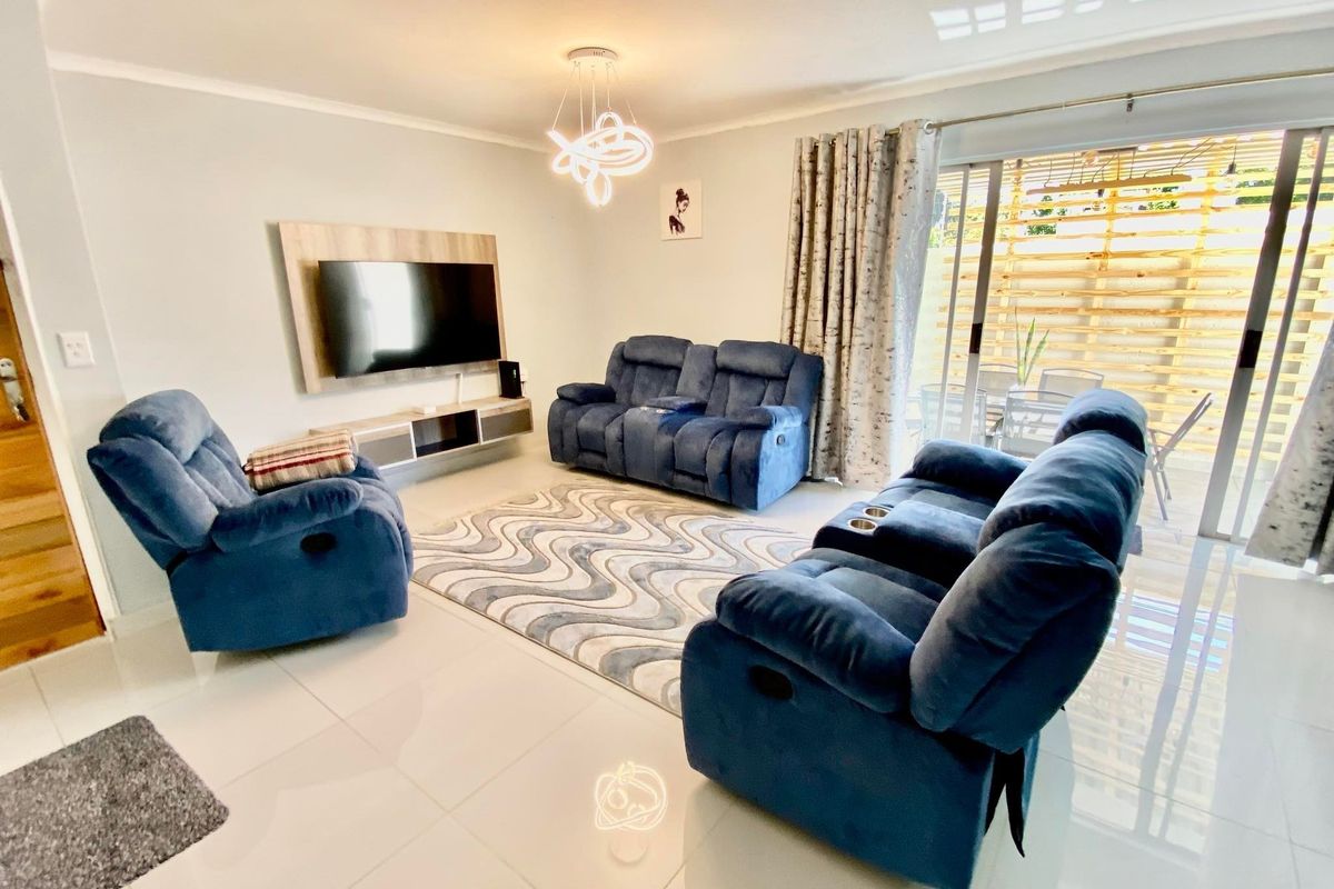 A bright and modern living room featuring tiled flooring, a built-in media console, and large sliding glass doors leading to an outdoor area.