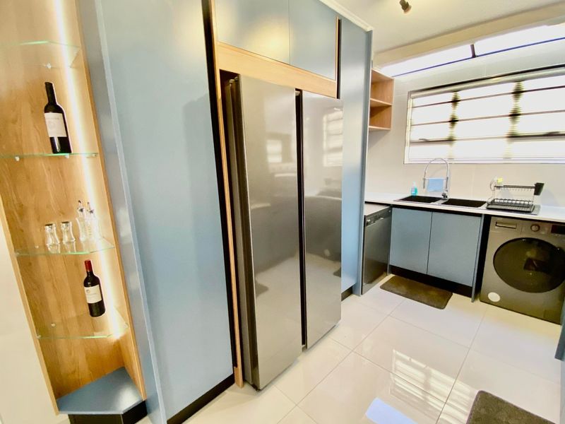 Modern kitchen featuring sleek blue cabinetry, integrated shelving, double sink, and tiled flooring with ample natural light.