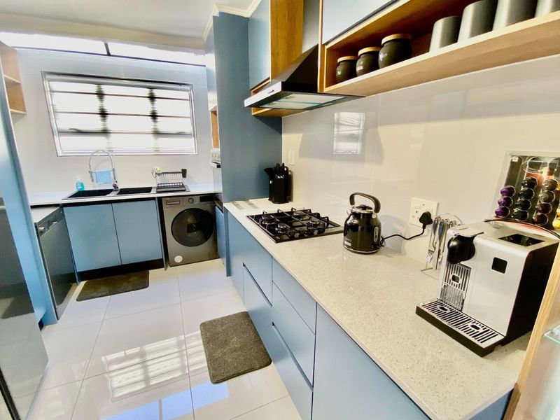 Modern kitchen featuring sleek blue cabinetry, stone countertops, a gas hob with extractor fan, and integrated space for laundry appliances.