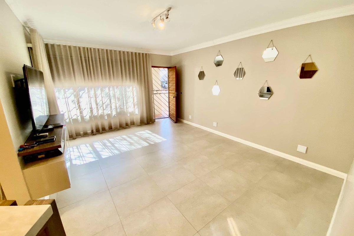 A bright living room featuring neutral tiled flooring, modern cornicing, and a security gate leading to the exterior.