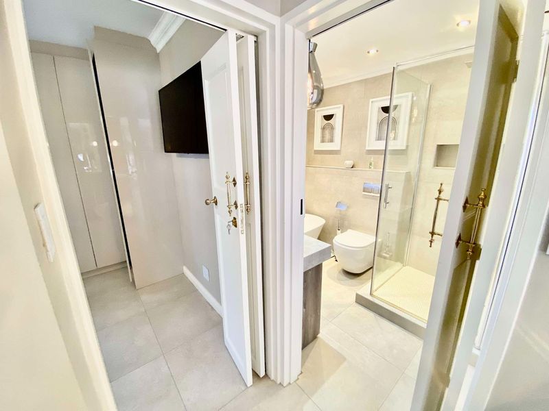 Modern bathroom featuring a walk-in glass shower, wall-hung toilet, and neutral tiling, adjacent to a dressing area with built-in cabinetry.