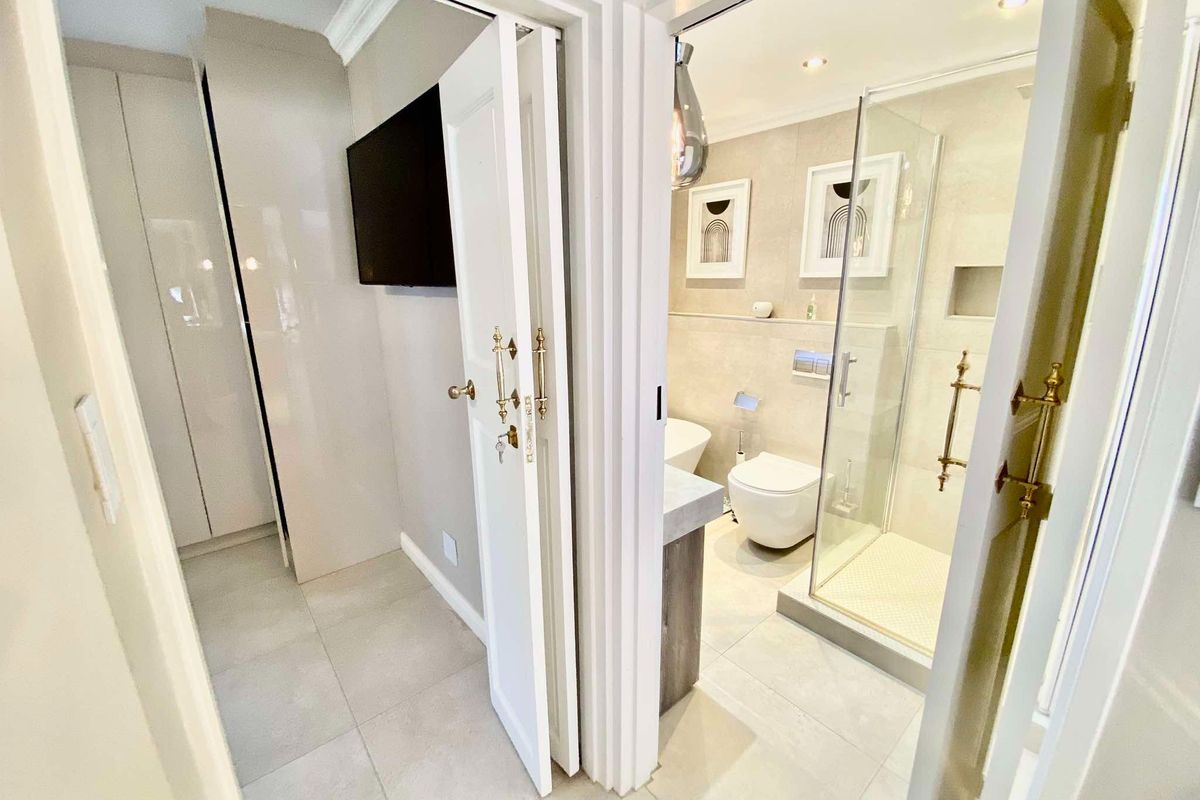 Modern bathroom featuring a walk-in glass shower, wall-hung toilet, and neutral tiling, adjacent to a dressing area with built-in cabinetry.