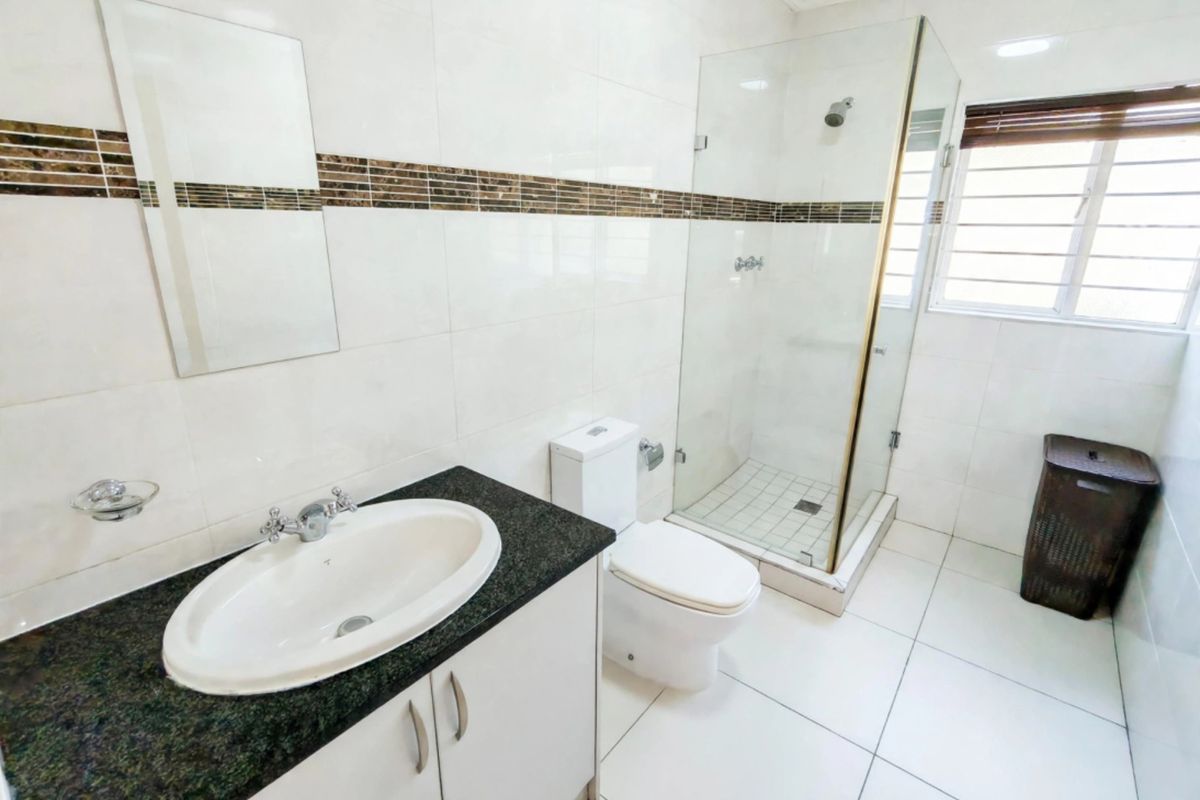 A clean, well-maintained bathroom featuring a granite-topped vanity, a glass-enclosed shower, and neutral wall and floor tiling.