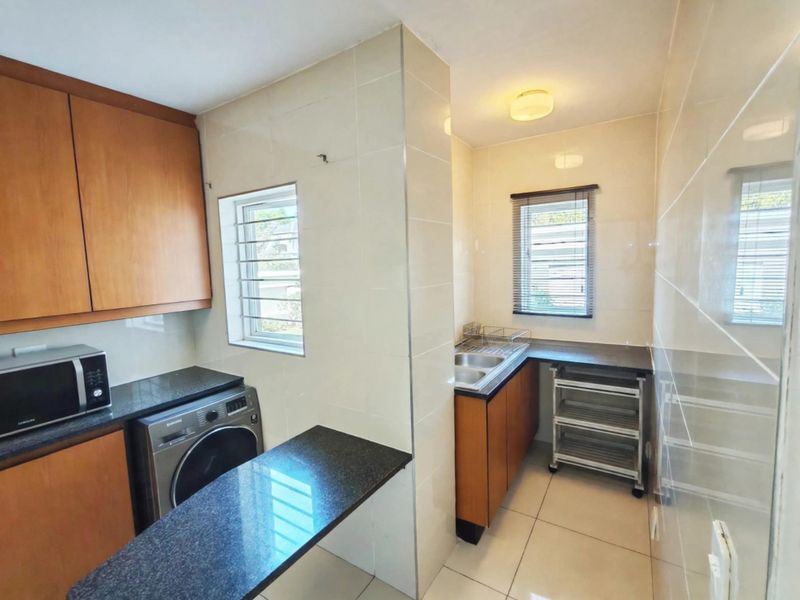 A functional scullery area featuring built-in wooden cabinetry, granite countertops, double sink, and tiled finishes, providing additional prep and utility space.