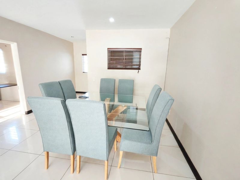 A bright and neutral dining area featuring large format floor tiles, recessed lighting, and venetian blinds, providing a clean and functional space.