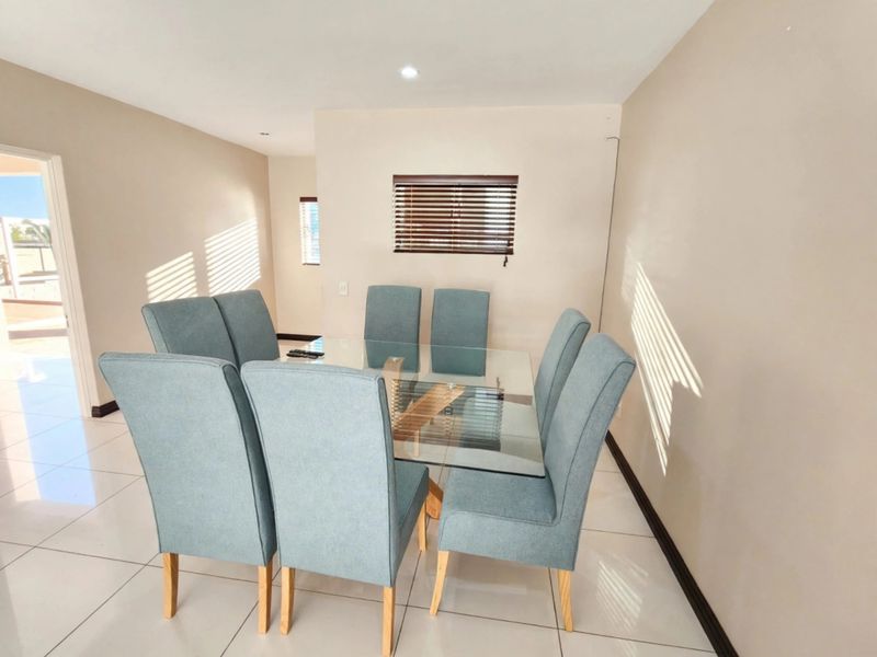 A bright dining room featuring neutral walls, large format floor tiles, and natural light filtered through venetian blinds.