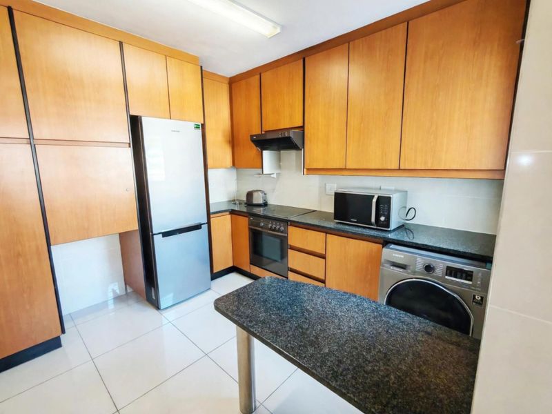 A functional kitchen featuring wooden cabinetry, granite countertops, a breakfast bar, and built-in appliances including an oven and extractor fan.