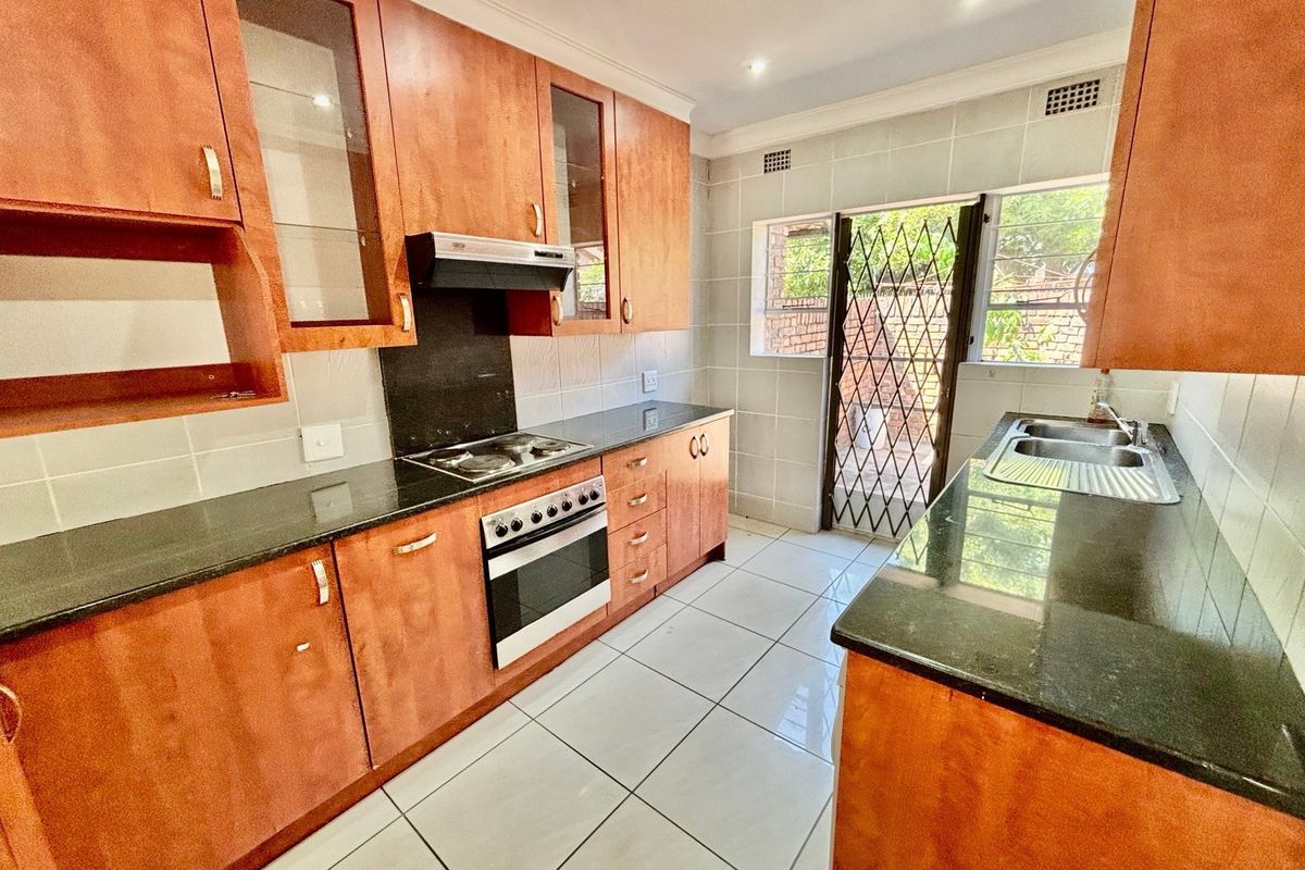 A functional kitchen featuring wooden cabinetry, granite countertops, a built-in oven with gas hob, and direct access to the exterior via a security gate.