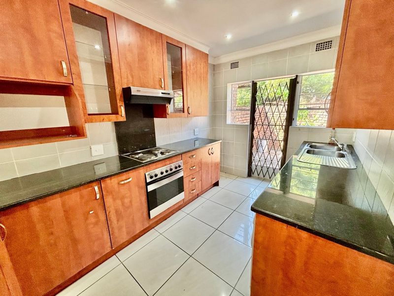 A functional kitchen featuring wooden cabinetry, granite countertops, a built-in oven with gas hob, and direct access to the exterior via a security gate.