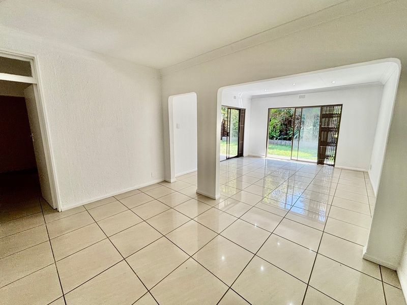Spacious open-plan living area featuring neutral ceramic floor tiles, recessed lighting, and large sliding glass doors providing direct access to the garden.