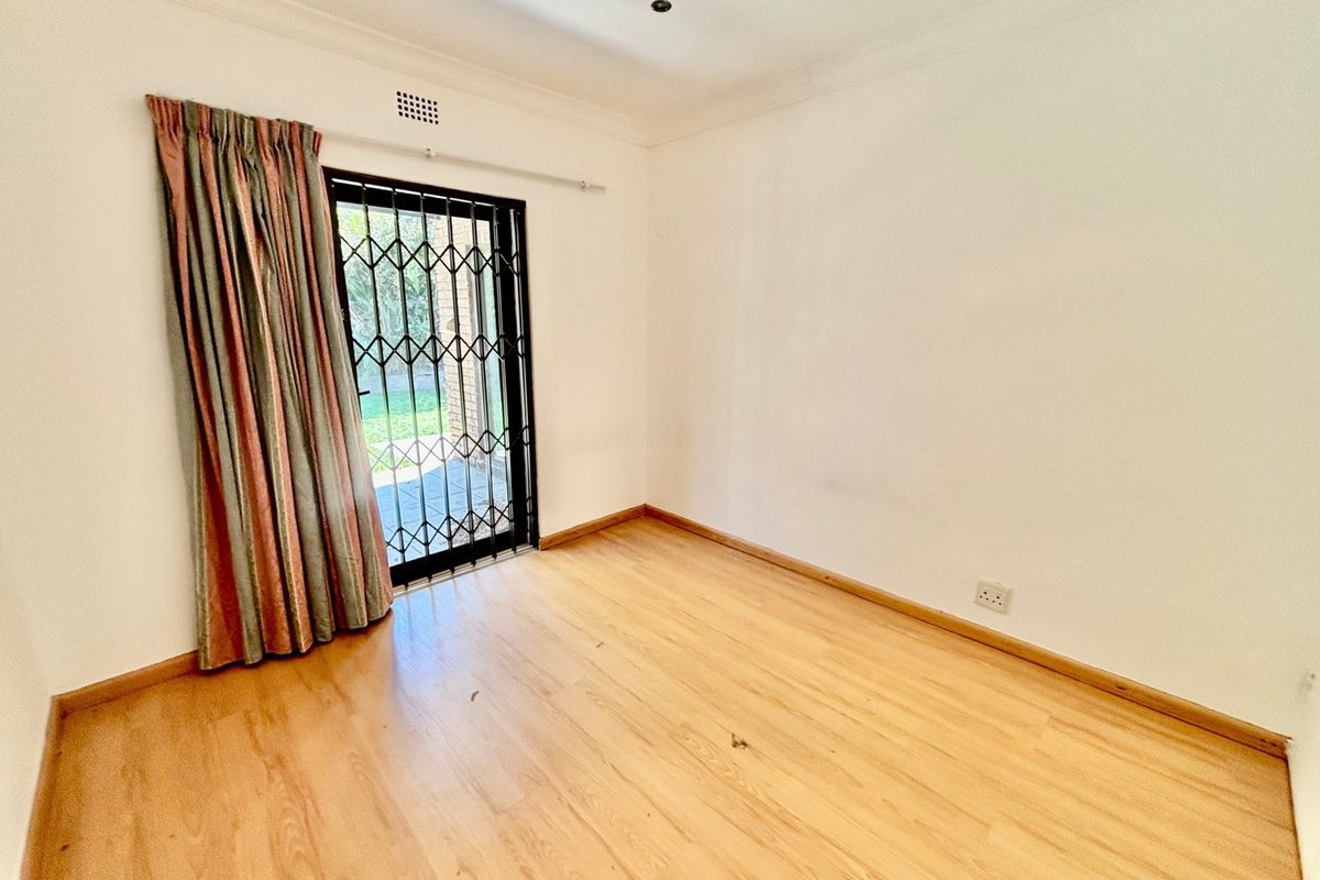An empty bedroom featuring laminate flooring, coving, and a sliding door with a security gate leading to the exterior.
