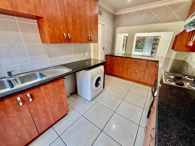 Functional kitchen featuring wood-finish cabinetry, granite countertops, tiled flooring, and a built-in electric hob with extractor fan.