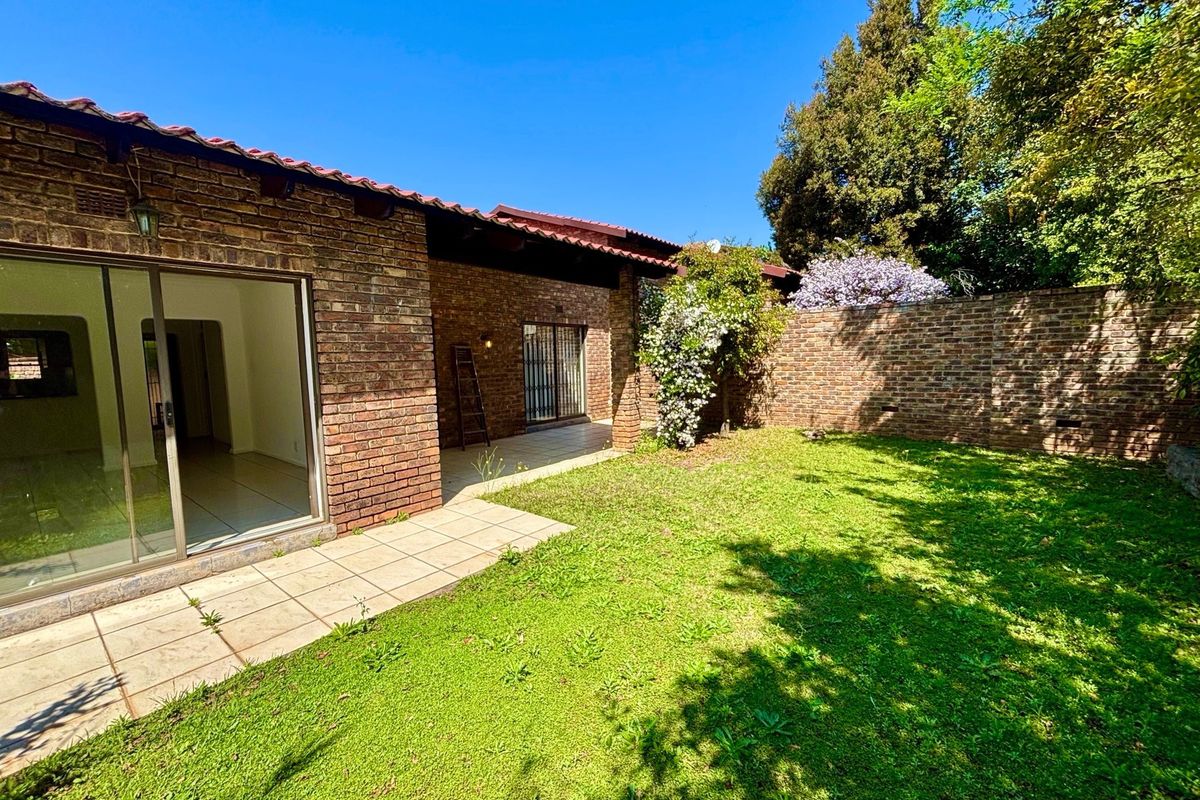 A private rear garden featuring a paved patio area, brick facade, and established lawn, accessible via sliding glass doors from the main living space.