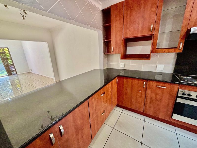 A functional kitchen featuring dark granite countertops, wood-finish cabinetry, and built-in appliances, with an open-plan layout connecting to the adjacent living area.