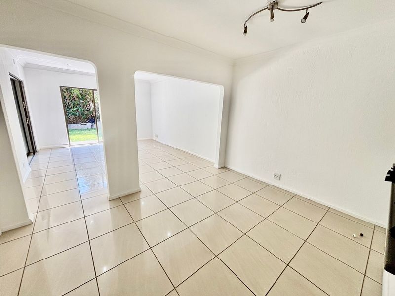 An empty, open-plan living area featuring neutral tiled flooring, white walls, and an archway leading to an adjacent space with garden access.